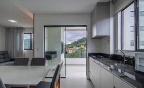 Een moderne keuken met een groot raam, een eethoek met een tafel en stoelen, en uitzicht op een groene heuvel.