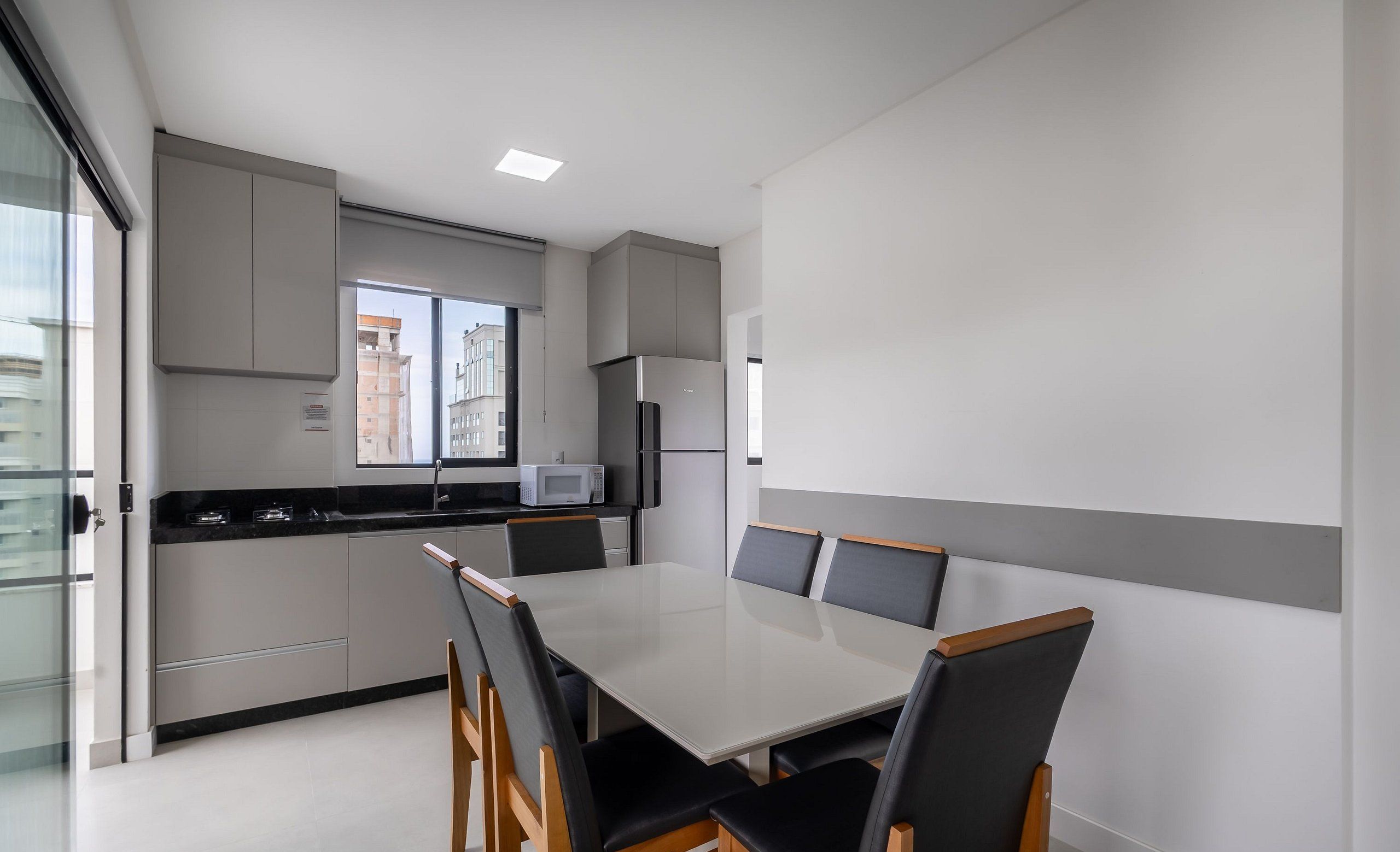 Uma cozinha moderna com área de refeições, apresentando uma mesa grande e cadeiras, um micro-ondas e uma geladeira.