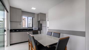 Uma cozinha moderna com área de refeições, apresentando uma mesa grande e cadeiras, um micro-ondas e uma geladeira.