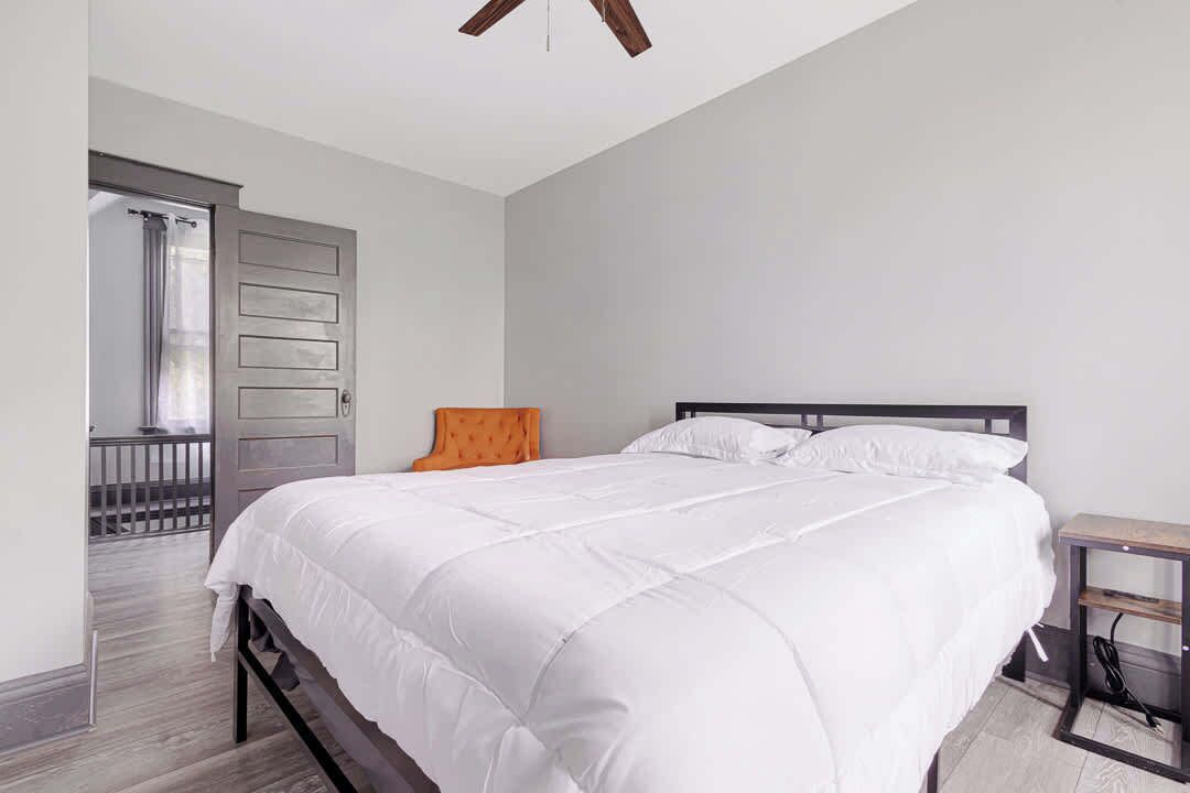 A bedroom with a large bed, a wooden chair, a nightstand, and a door leading to a balcony.