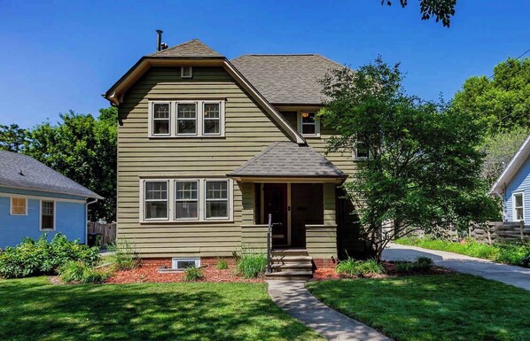 A two-story house with a front porch, a chimney, and a small front yard with a pathway.