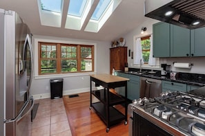 A modern kitchen with skylights, a stainless steel refrigerator, a gas stove, and teal cabinets.