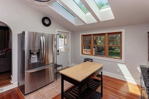 A modern kitchen with a stainless steel refrigerator, a wooden table, and skylights.