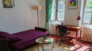 A room with a bed, a desk, a chair, a radiator, and a window with curtains. - Le soleil rayonnant: bed and breakfast at the foot of Vézelay hill, (Asquins)