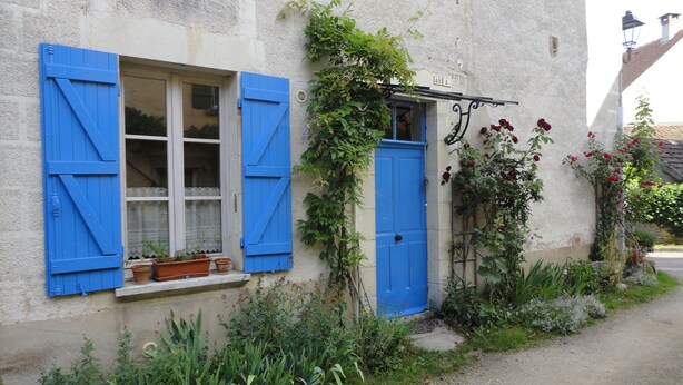 A rustic building with blue shutters, a small window with potted plants, and a door with a metal gate. - Le soleil rayonnant: bed and breakfast at the foot of Vézelay hill, (Asquins)