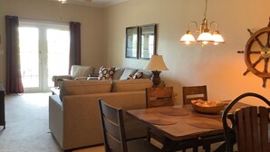 A living room with a sofa, a dining table with chairs, a ceiling fan, and a ship's wheel decoration. - Sunsets, Canal Front, FISH, FISH, FISH!  Suwannee Cove - Unit 207, Boat Slip 23 (Suwannee)