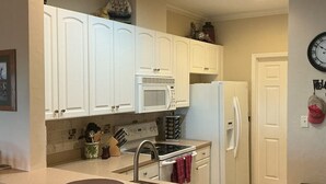A kitchen with white cabinets, a microwave, stove, and a refrigerator. There are two bar stools and a clock on the wall. - Sunsets, Canal Front, FISH, FISH, FISH!  Suwannee Cove - Unit 207, Boat Slip 23 (Suwannee)