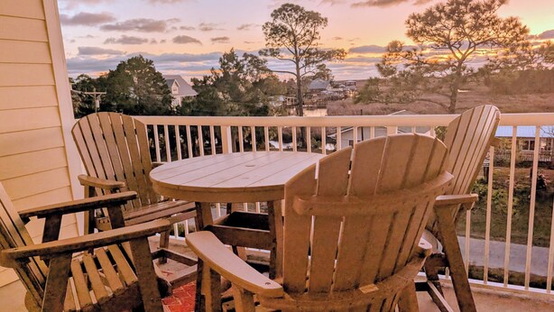 A wooden deck with Adirondack chairs and a table, overlooking a residential area with houses and trees. - Sunsets, Canal Front, FISH, FISH, FISH!  Suwannee Cove - Unit 207, Boat Slip 23 (Suwannee)