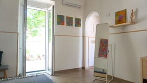 Ein Zimmer mit einer Schiebeglastür, die auf einen Balkon führt, einem stehenden Spiegel und drei abstrakten Bildern an der Wand.