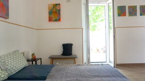 Ein Schlafzimmer mit Bett, einer Bank, einer Tasche und einer Tür zu einem Balkon.