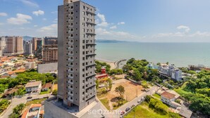 Ein Hochhaus mit mehreren Stockwerken, umgeben von Grünflächen und einem Strand im Hintergrund.