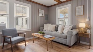 A living room with a grey sofa, a wooden coffee table, a grey armchair, and a wooden nightstand with a lamp.