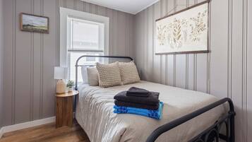 Ein Schlafzimmer mit Bett, Fenster, Nachttisch mit Lampe und einem Wandbild.
