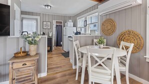 Eine kompakte Küche mit weißen Geräten, ein Essbereich mit weißen Stühlen und einer Holzbalkendecke.