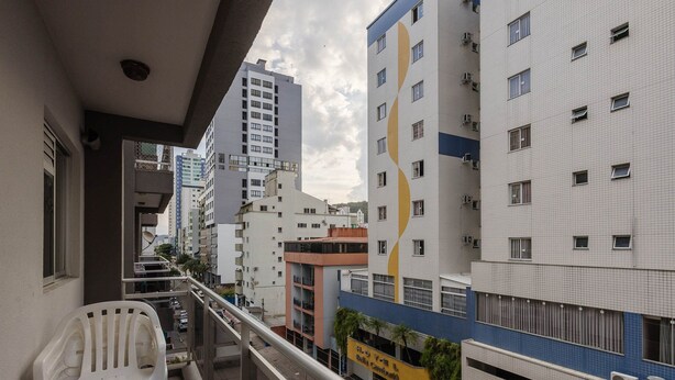 A balcony with white plastic chairs, a view of adjacent buildings, and a sign for "SEUZONE SEU LUGAR FORA DE CASA".