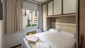 A hotel room with a bed, a window with curtains, a view of the city, and a built-in wardrobe.