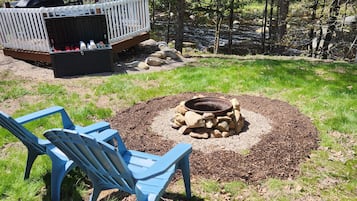 A backyard with a fire pit, two blue chairs, and a white deck.