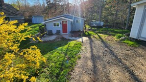 A small house with a red door, a porch with two chairs, and a deck.