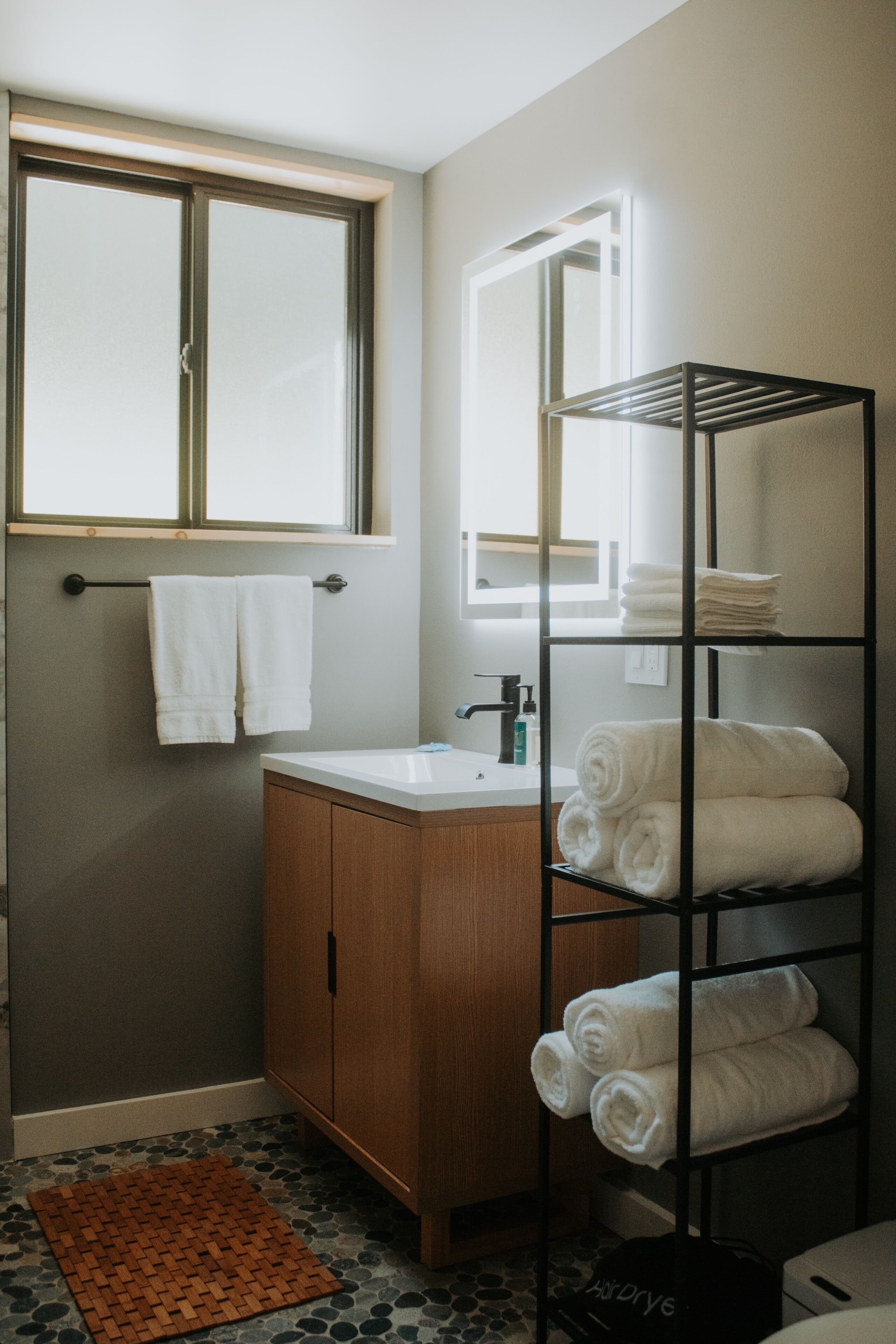 A bathroom with a wooden cabinet, a white sink, a towel rack, a metal towel rack, and a window.
