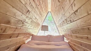 A cozy wooden cabin with a bed and a small window at the end. - Cabin 1: Unplug, unwind, unearth your peace at The Wildflower. (Princeton)