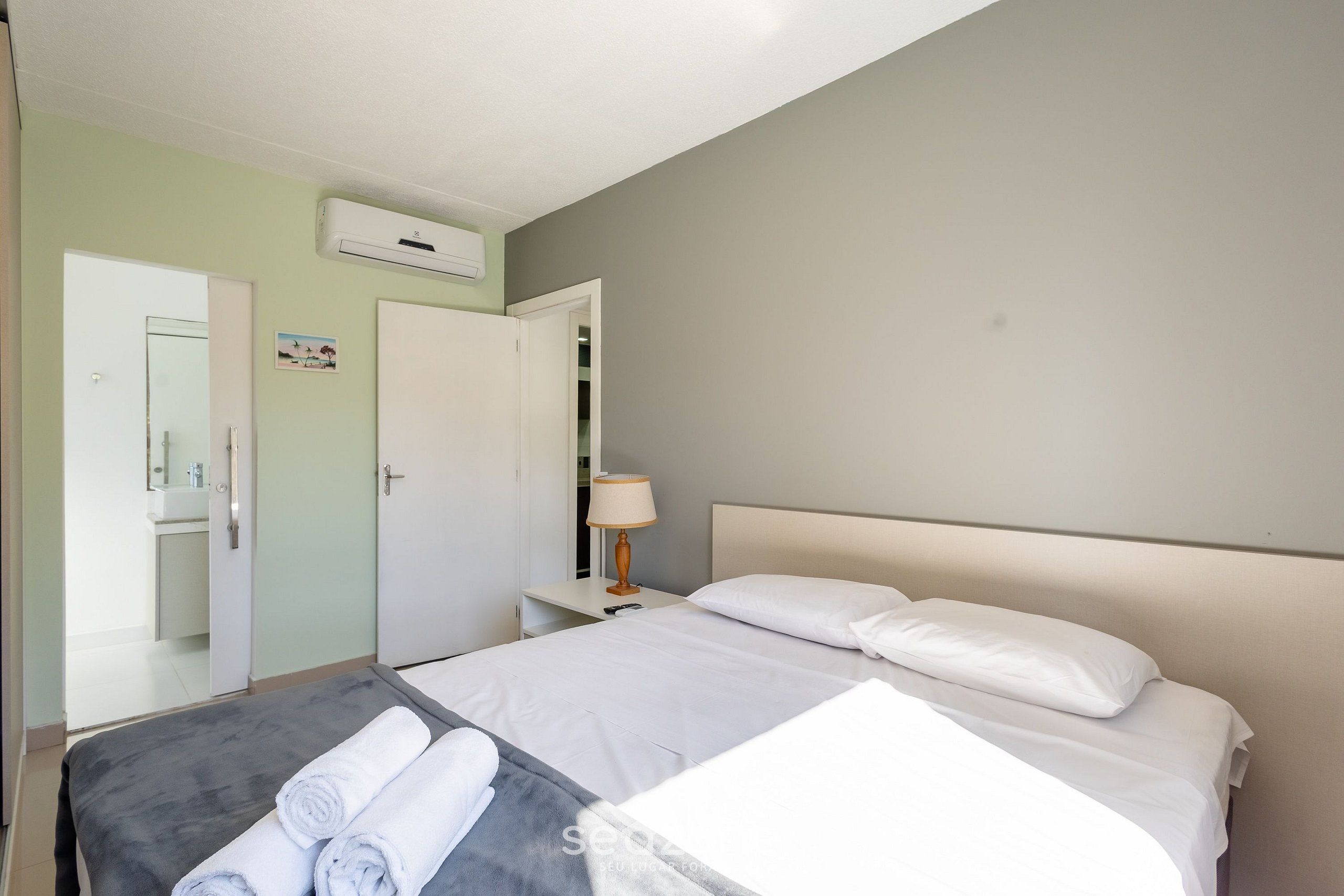 A hotel room with a bed, a bedside table with a lamp, a mirror, and a wardrobe.