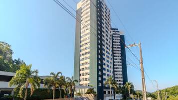 A tall residential building with multiple balconies, surrounded by parked cars and palm trees.