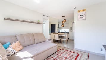 Una sala de estar moderna con un sofá color beige, un tapete estampado y una cocina al fondo.