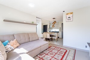 A modern living room with a beige sofa, a patterned rug, and a kitchen in the background. - Beautiful Apartment in Building With Pool Mpb0034 (Itajai)