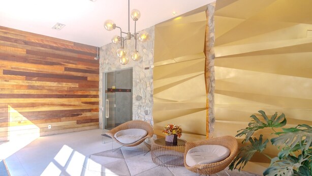 A modern interior with wooden panel walls, a stone accent wall, and a glass door leading to a bathroom. There are two wicker chairs and a small table with a vase of flowers. - Beautiful Apartment in Building With Pool Mpb0034 (Itajai)
