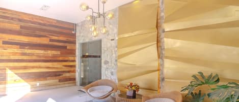 A modern interior with wooden panel walls, a stone accent wall, and a glass door leading to a bathroom. There are two wicker chairs and a small table with a vase of flowers.