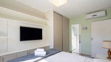 Habitación de hotel con cama, televisor de pantalla plana montado en la pared, zona de ducha y aire acondicionado.