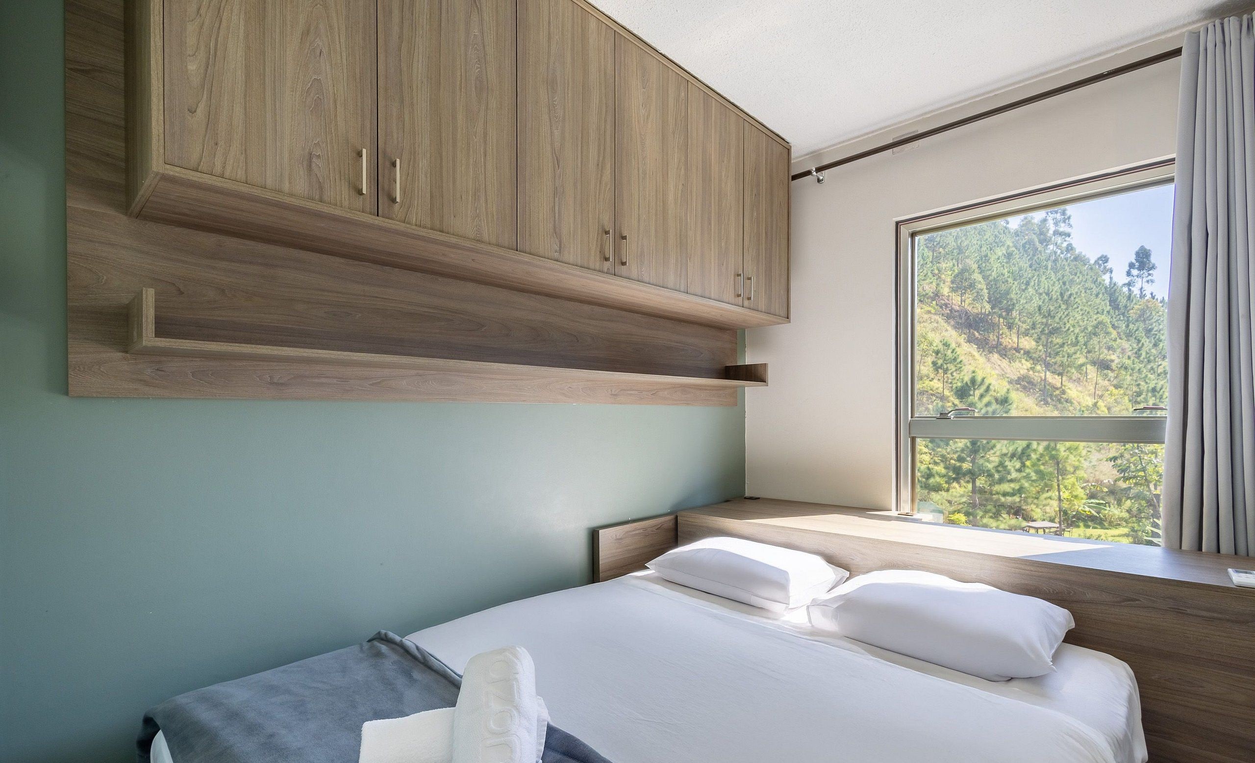 Un dormitorio con una cama, un armario de madera y una ventana con vistas a árboles.