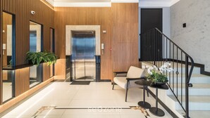 A modern lobby with a wooden panel wall, an elevator, a staircase with a black railing, and a seating area with a plant. - 3 Bedroom Apartment 130m From the Beach Mmp0137 (Itapema)