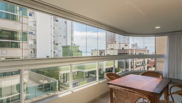A balcony with a dining table and chairs, large windows offering a view of surrounding buildings. - 3 Bedroom Apartment 130m From the Beach Mmp0137 (Itapema)