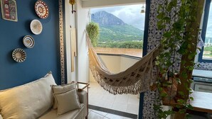 Un salon avec un mur bleu, un hamac, un canapé, une table basse et une vue sur les montagnes.