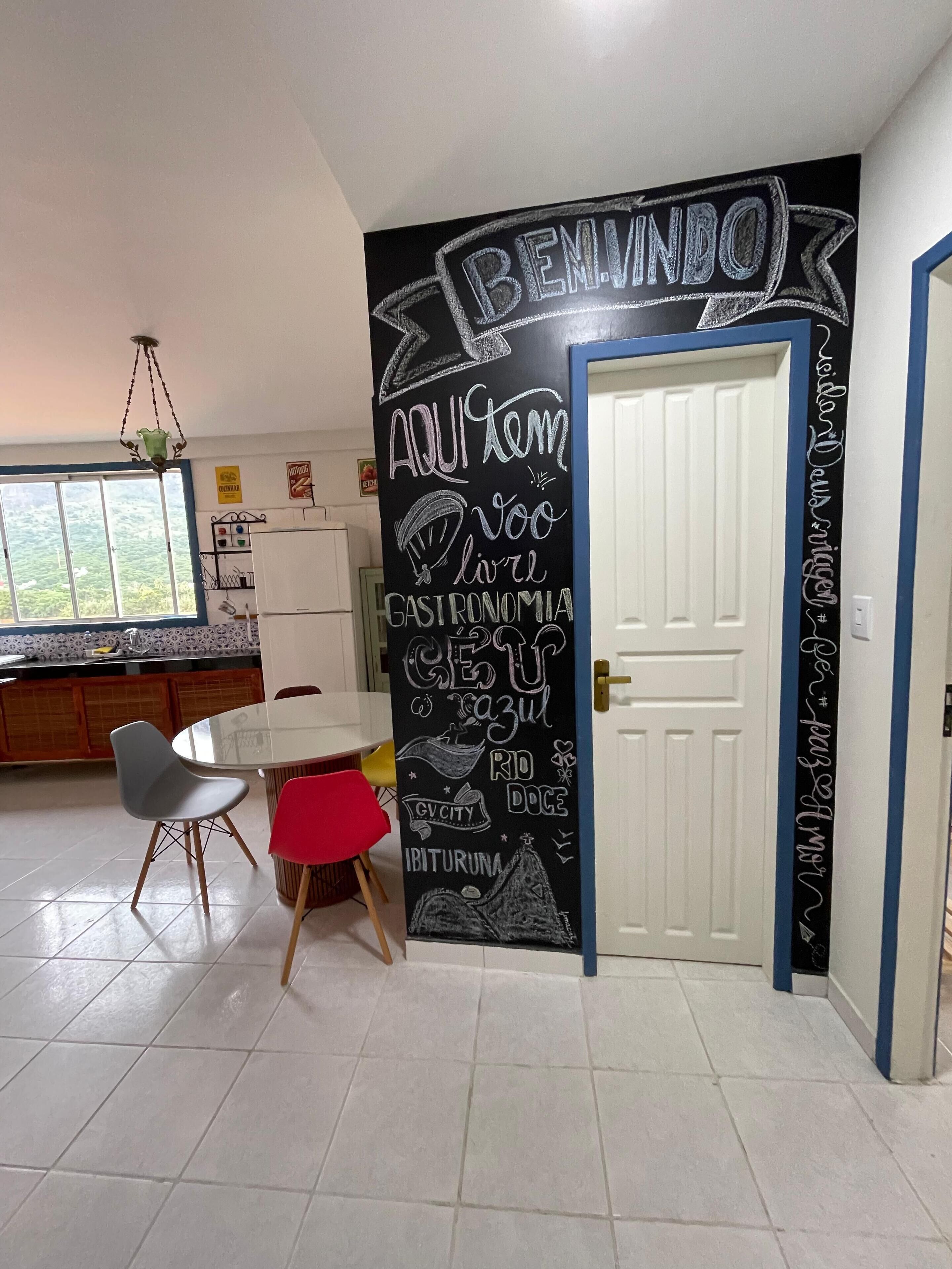 Une cuisine avec un mur recouvert d’un tableau noir, une table à manger avec des chaises et un réfrigérateur.