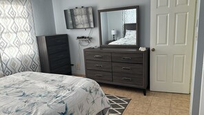 Une chambre à coucher avec un lit, une commode, un miroir et une porte.