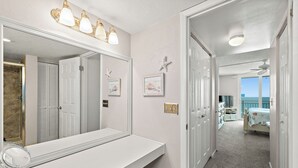 A bathroom with a large mirror, vanity, and a ceiling fan.