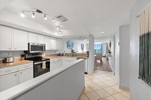 A modern kitchen with white cabinetry, a central island, stainless steel appliances, and a view to the living area. - Oceanfront 2BR Condo Bright Breezy Beachfront Indian Harbour Beach, 606 (Indian Harbour Beach)