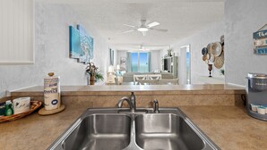 A kitchen with a double sink, a ceiling fan, and a view of a dining area.