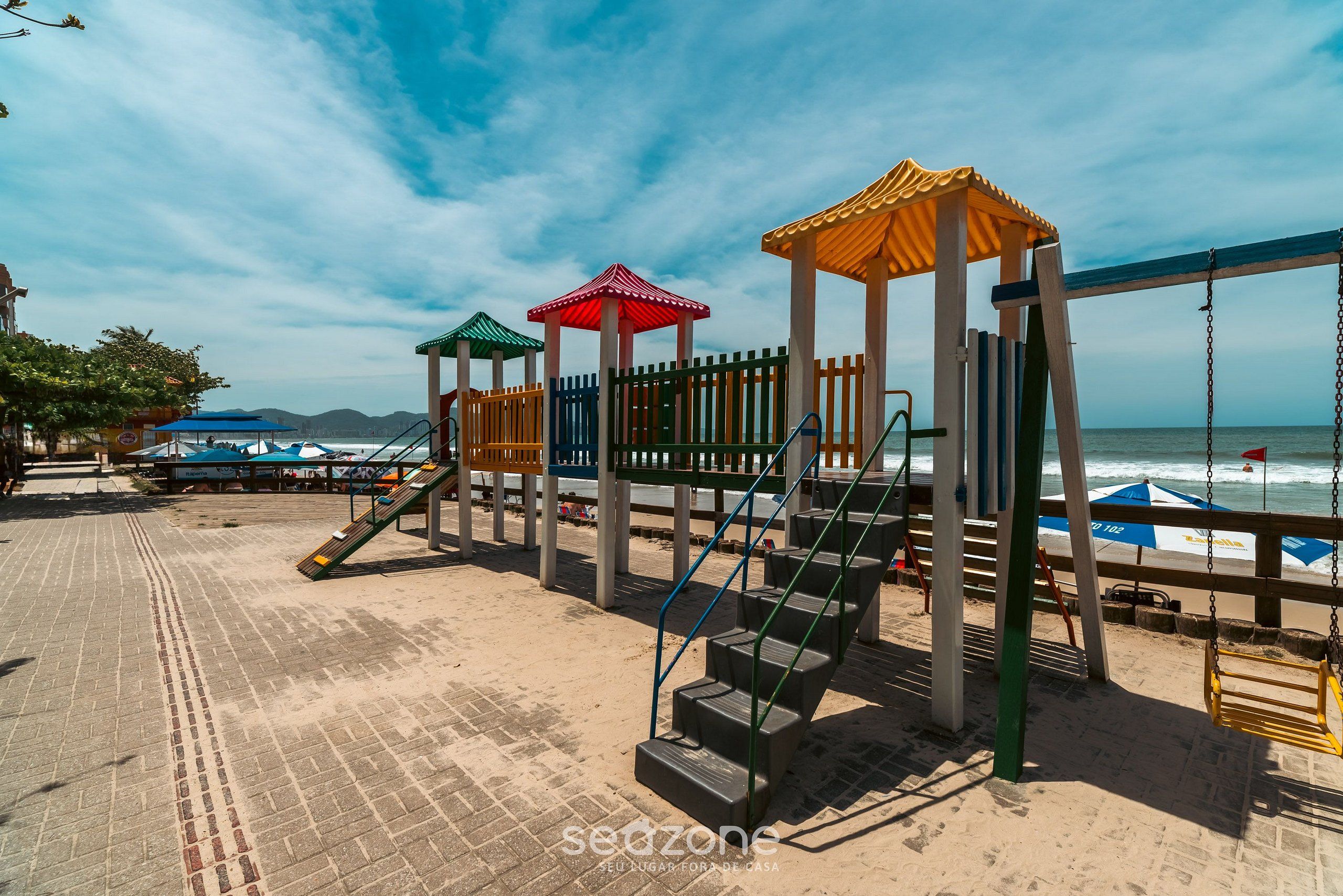A beachside playground with a wooden fence, a set of stairs, and a swing set.