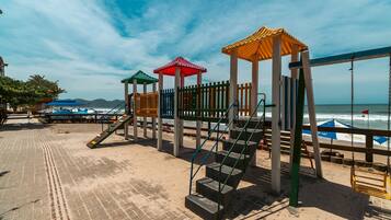A beachside playground with a wooden fence, a set of stairs, and a swing set.