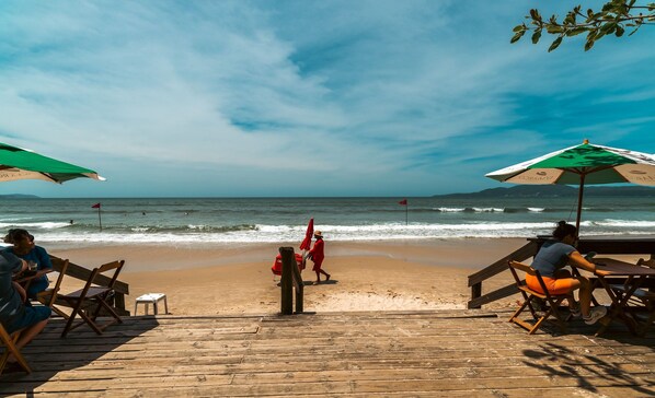 Une terrasse en bois avec des chaises de plage et des parasols, donnant sur l’océan.