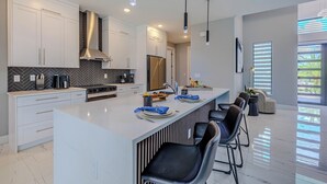 A modern kitchen with white cabinetry, a central island, and black bar stools. - Sleeps 6, Heated pool, Outdoor lounge - Stars Vacation Rentals (Cape Coral)