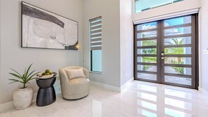 A spacious room with a large abstract painting, a potted plant, a modern chair, and a large sliding glass door leading to an outdoor area. - Sleeps 6, Heated pool, Outdoor lounge - Stars Vacation Rentals (Cape Coral)