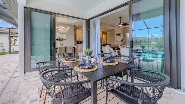 An outdoor dining area with a glass-enclosed patio, black metal chairs, and a table set with plates and glasses. - Sleeps 6, Heated pool, Outdoor lounge - Stars Vacation Rentals (Cape Coral)