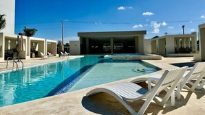 A swimming pool with lounge chairs, a covered seating area, and a clear blue sky.