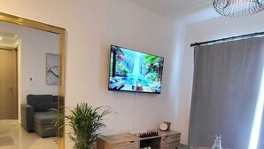 A modern living room with a flat-screen TV, a sofa, a coffee table, and a potted plant.
