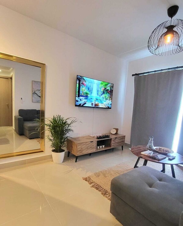 Ein modernes Wohnzimmer mit Flachbildfernseher, einer Couch, einem Couchtisch und einer Topfpflanze.