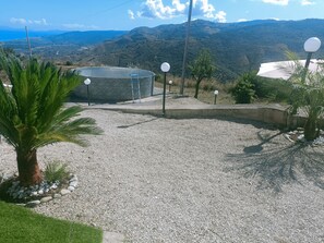 Un espacio con grava, una estructura de piedra, una palmera y vistas a colinas distantes.